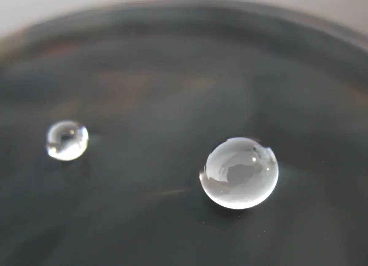 L'acqua con due gocce che si riflettono, evidenziando effetti di superficie e trasparenza.