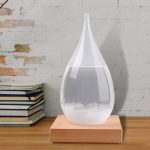 Acquario decorativo a forma di goccia in vetro trasparente, posizionato su una base in legno naturale, ideale per ambienti moderni e per appassionati di oggetti scientifici e decorativi.