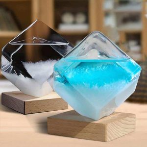 Due vasi decorativi in vetro con liquidi colorati, uno nero e uno azzurro, posizionati su basi di legno, ideali come oggetti di decorazione scientifica e per ambienti moderni.
