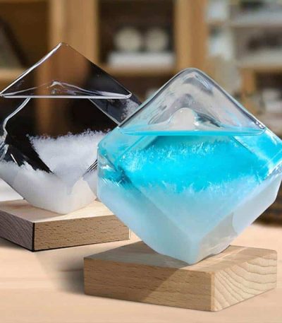 Due vasi decorativi in vetro con liquidi colorati, uno nero e uno azzurro, posizionati su basi di legno, ideali come oggetti di decorazione scientifica e per ambienti moderni.