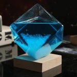 Vaso di cristallo trasparente con liquido blu e cristalli di sale, posizionato su base di legno, decorazione scientifica elegante e moderna.