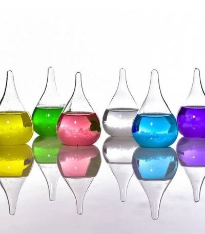 Vasi di vetro colorati con liquidi di diversi colori, riflessi su superficie lucida, decorazioni scientifiche e artistiche.