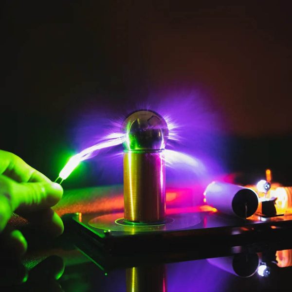 Immagine di una pila di Tesla con scarica elettrica colorata, illuminata da luci viola, verdi e blu, che evidenzia l'effetto di alta tensione e fenomeni elettrici.