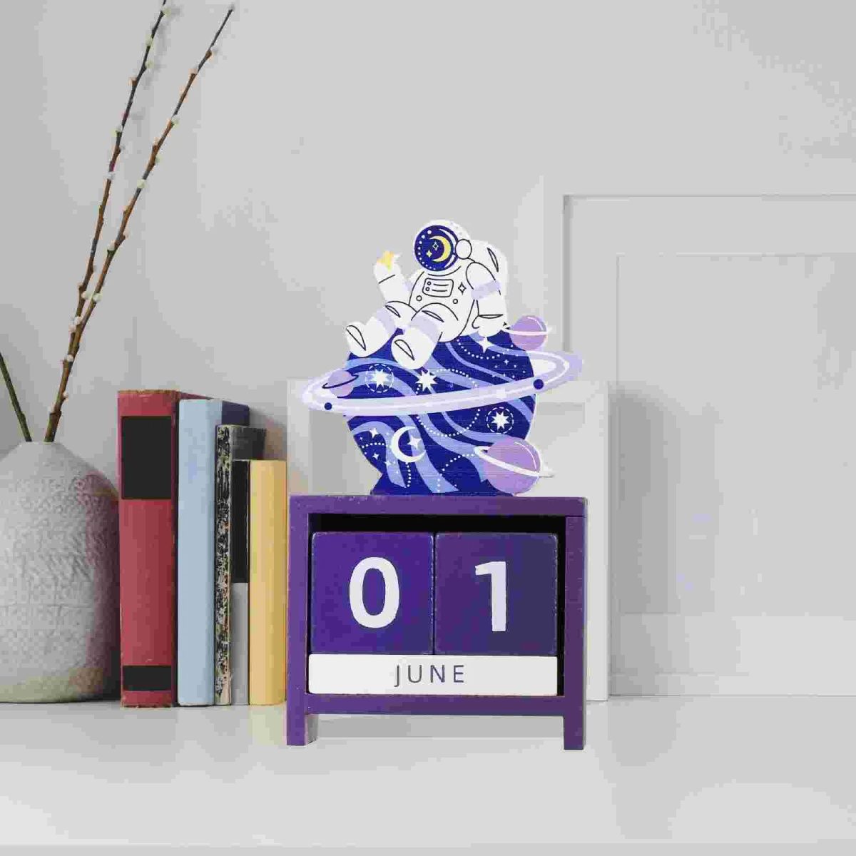 Decorazione di un astronauta in miniatura su un calendario a blocchi con data 1 giugno, con sfondo minimalista e libri, ideale come decorazione scientifica.