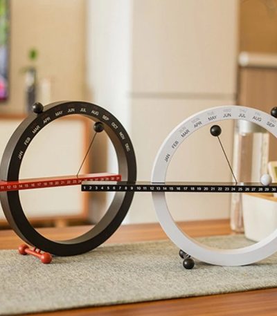 Due orologi scientifici con calendario perpetuo, uno nero e uno bianco, posizionati su un tavolo in un ambiente domestico. Ideali come decorazioni educative e oggetti da collezione.