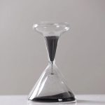 Sabbia nera in un orologio a clessidra di vetro, rappresenta il passare del tempo e l'elemento scientifico.