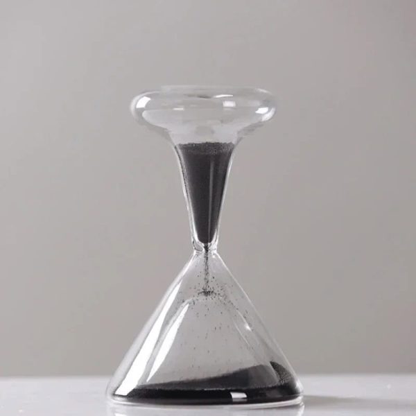 Sabbia nera in un orologio a clessidra di vetro, rappresenta il passare del tempo e l'elemento scientifico.