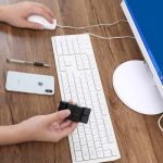 Mani che manipolano un cubo di Rubik vicino a tastiera, mouse e smartphone su scrivania in ambiente di lavoro o studio.