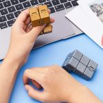 Due cubi di plastica colorati, uno dorato e uno grigio, posizionati su una superficie blu accanto a un laptop e fotografie, ideali come decorazioni scientifiche o oggetti da collezione.