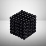 Pallina nera in un cubo 3D, rappresentazione di un oggetto scientifico decorativo, con superficie liscia e lucida, disposto in modo ordinato e simmetrico.