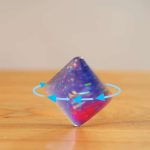 Cubo di vetro luminoso con effetti iridescenti e frecce blu che indicano rotazione, ideale come decorazione scientifica o oggetto da collezione.