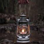 Lampada a olio vintage in un ambiente naturale, con fiamma accesa, immersa in un paesaggio boschivo, simbolo di avventura e scoperta.
