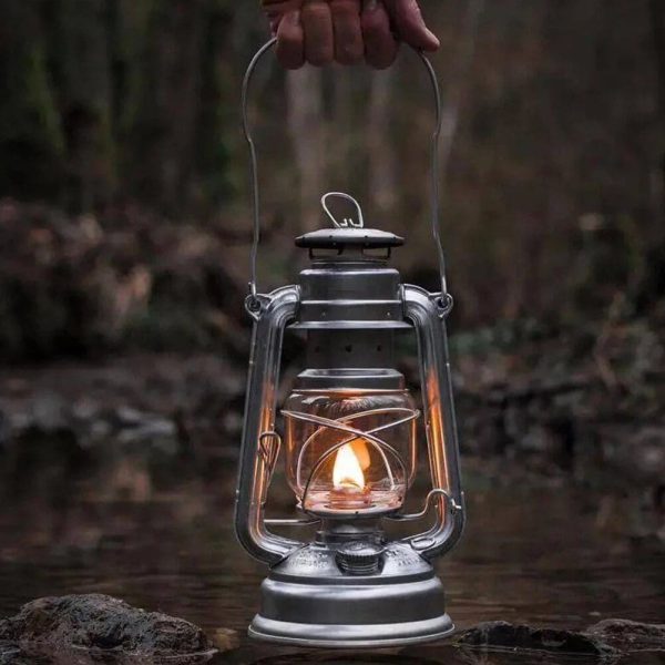 Lampada a olio vintage in un ambiente naturale, con fiamma accesa, immersa in un paesaggio boschivo, simbolo di avventura e scoperta.