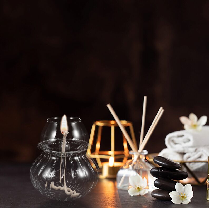 Vaso di vetro con candela accesa, pietre nere, fiori bianchi e oggetti decorativi zen, ideale per ambienti di relax e benessere.