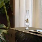 Lampada a olio vintage in vetro trasparente su scrivania moderna con libro aperto, decorazione scientifica elegante, ambiente luminoso e accogliente.