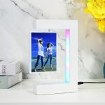Fotografia di una lampada decorativa con schermo digitale che mostra un'immagine di due donne sulla spiaggia, in piedi e che si guardano, in un ambiente moderno e luminoso.