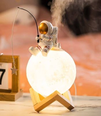 Astronauta in tuta spaziale seduto sulla lampada a forma di luna, decorazione scientifica originale e originale per ambienti a tema spaziale o scientifico.