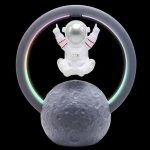 Figura di astronauta in stile giocattolo con dettagli rossi, circondato da un alone di luci colorate, sopra una replica della Luna, ideale come decorazione scientifica originale.