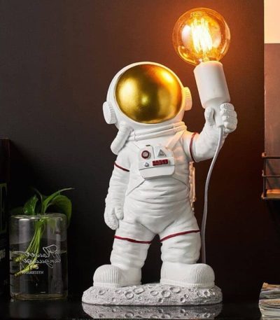 Statua di astronauta con casco dorato e lampada a forma di lampadina accesa, decorazione scientifica originale per ambienti moderni e tematici.