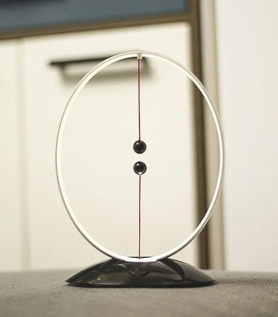 Pêndulo Newton con sfera nera e cerchio in vetro, perfetto come decorazione scientifica o oggetto educativo, su superficie nera con sfondo neutro.