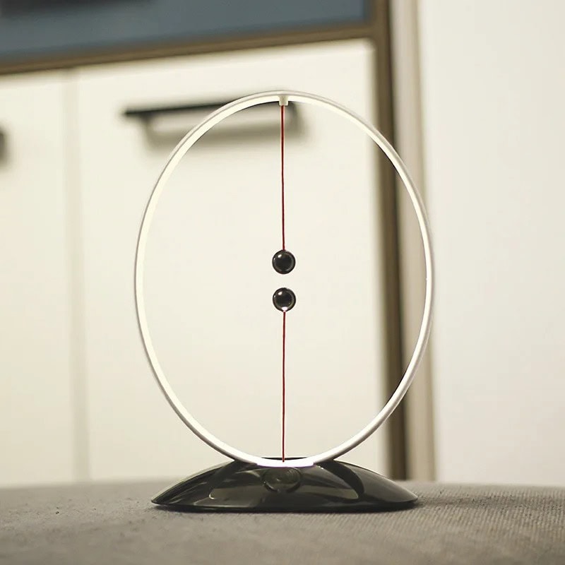 Pêndulo Newton in vetro e metallo Pêndulo Newton con sfera nera e cerchio in vetro, perfetto come decorazione scientifica o oggetto educativo, su superficie nera con sfondo neutro.