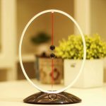 Péndolo di Newton con sfondo decorativo, mostra le sfere che oscillano lungo un arco luminoso, simbolo di fisica e scienza. Perfetto come oggetto decorativo scientifico per ambienti educativi o modern.