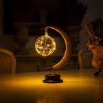 Oggetto decorativo luminoso con forma di pallina e simbolo della luna, decorato con rete di luci dorate, ideale per ambienti scientifici o decorazioni eleganti.