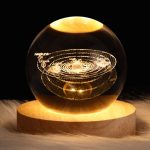 Modello in cristallo del sistema solare con pianeti come Mercurio, Venere, Terra, Marte, Giove, Saturno, Urano e Nettuno, illuminato e posizionato su base di legno.