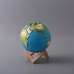Modello in miniatura della Terra su supporto di legno, rappresenta il nostro pianeta con continenti e oceani dettagliati, ideale come decorazione scientifica.