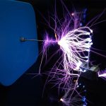Immagine di una scarica elettrica visibile come una scintilla di plasma con luci viola e blu, che si propaga tra due elettrodi in un ambiente di laboratorio.
