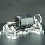 Modello di motore scientifico in miniatura con parti trasparenti e dettagli metallici, ideale come decorazione o oggetto da collezione scientifica.
