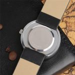 Orologio con cinturino beige e nero, vista dal retro, su superficie nera con cioccolatini.