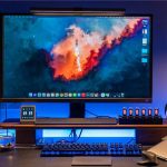 Schermo computer con immagine di spazio e razzo in lancio, accompagnato da accessori come tastiera, mouse, orologio digitale e bobine di cavi USB, ambientato in un'area di lavoro moderna e tecnologica.