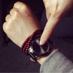 Orologio scientifico digitale con pulsante di controllo, indossato da una persona con braccialetti rossi, in un ambiente interno.