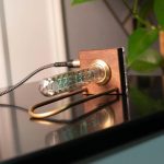Termometro a tubo di vetro con display digitale, dispositivo scientifico per misurare la temperatura con precisione, posizionato su una superficie nera vicino a una pianta verde.
