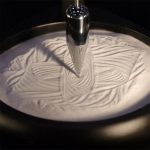 Punta di penna che crea disegni su una superficie di crema o schiuma, ideale per decorazioni scientifiche e artistiche.
