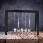 Péndolo di Newton in metallo lucido, oggetto decorativo scientifico con cinque sfere sospese, ideale per arredamento da studio o laboratorio.