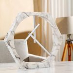 Orologio da tavolo decorativo in marmo con struttura a forma di esagono e lancette minimaliste, perfetto come oggetto di arredamento scientifico o moderno.
