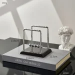 Pendolo di Newton decorativo in metallo con sfera in acciaio, perfetto come oggetto di arredamento scientifico e decorativo per scrivanie e studi.