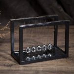 Péndolo di Newton con sfere di vetro e struttura metallica nera, perfetto come decorazione scientifica o oggetto educativo.