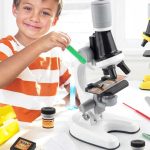 Bambino che utilizza un microscopio da laboratorio con provette e strumenti scientifici, in un ambiente educativo e stimolante.