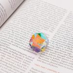 Immagine di una molecola di cristallo colorato con dettagli vivaci e trasparenza, posizionata su una pagina di libro aperto, evidenziando la bellezza delle decorazioni scientifiche.