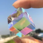 Pezzo di cristallo decorativo trasparente con riflessi iridescenti, tenuto tra le dita contro il cielo azzurro.