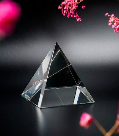 Piccola piramide di cristallo trasparente con riflessi luminosi su sfondo scuro, decorazione scientifica elegante e moderna.