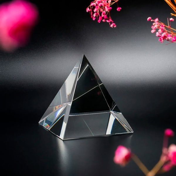 Piccola piramide di cristallo trasparente con riflessi luminosi su sfondo scuro, decorazione scientifica elegante e moderna.