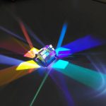 Cristallo trasparente che riflette luci di vari colori, creando effetti di luce e ombra su uno sfondo scuro. Perfetto come decorazione scientifica o oggetto da collezione.