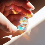 Cristallo colorato e riflettente in mano, con giochi di luce e riflessi arcobaleno, perfetto come decorazione scientifica o oggetto da collezione.