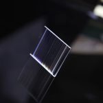 Piastra di vetro trasparente con riflessi iridescenti, sospesa in aria, su sfondo scuro. Perfetta come decorazione scientifica o oggetto di design innovativo.