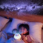 Bambina che guarda il cielo stellato proiettato sul soffitto, creando un'atmosfera magica e rilassante nella stanza. Decorazione scientifica che ispira sogni e curiosità sull'universo.
