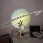 Proiezione di Saturno e ombra sulla parete con oggetti decorativi e libri.